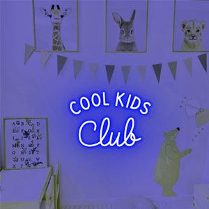 May include: Blue neon sign with the text "COOL KIDS CLUB" in a white cursive font. The sign is hanging on a wall with a light purple background.