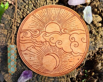 May include: A circular wooden tray with an engraved design of a sun, moon, and clouds. The tray is on a tree stump with crystals around it.