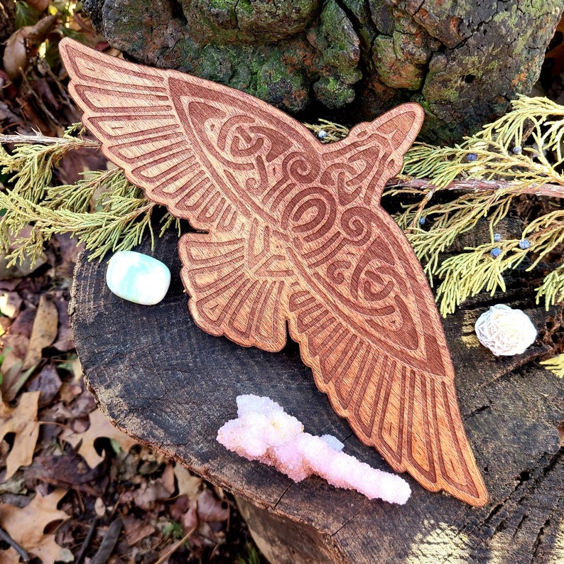 May include: A wooden carving of a stylized raven with intricate details. The carving is in a natural wood tone and has a rustic feel.