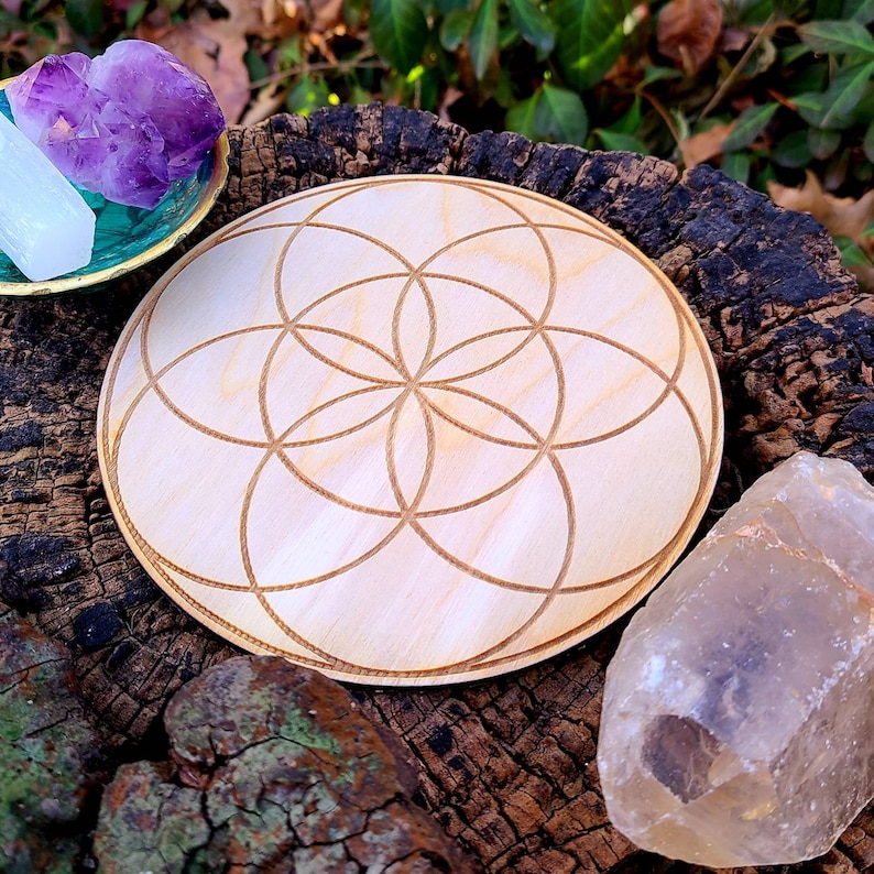 Peut inclure: Une plaque ronde en bois clair avec un motif de Fleur de Vie grav&eacute; au laser. La plaque est entour&eacute;e de cristaux, dont de l'am&eacute;thyste et du quartz. La plaque mesure environ 15 cm de diam&egrave;tre.
