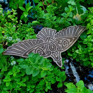 May include: A wooden carving of a stylized bird with intricate details, set against a backdrop of green foliage.