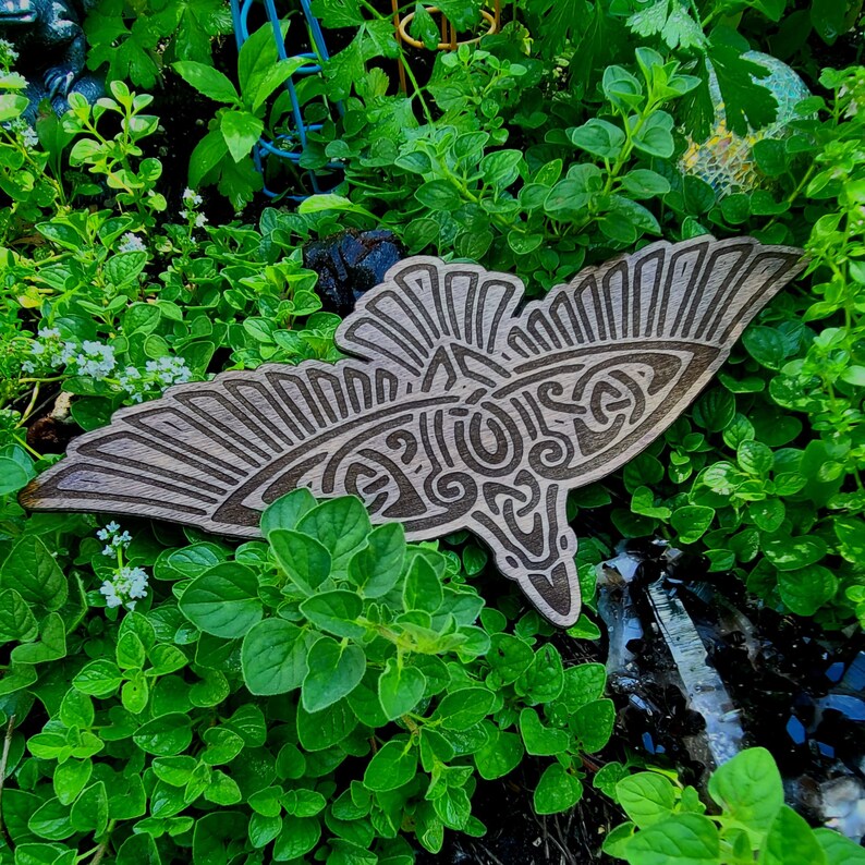 May include: A wooden carving of a stylized bird with intricate details, set against a backdrop of green foliage.