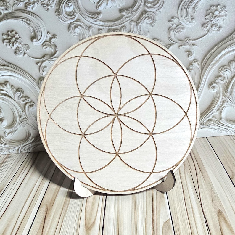 Peut inclure: Un objet d&eacute;coratif rond en bois clair avec un motif g&eacute;om&eacute;trique. Le motif pr&eacute;sente des cercles qui s'entrecroisent, cr&eacute;ant un motif floral. La pi&egrave;ce est soutenue par un petit support en bois.