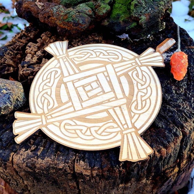 May include: A wooden Celtic knot cross with a woven design, resting on a tree stump. The cross is light brown and has a circular shape with a knot pattern around the edges.