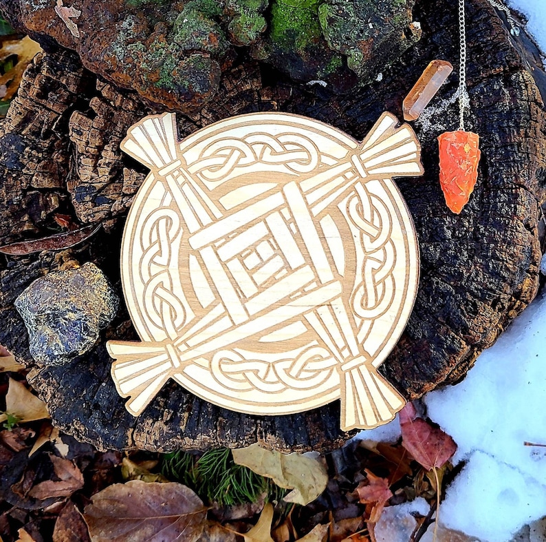 May include: A circular wooden board with a Celtic knot design and a woven pattern in the centre. The board is on a tree stump with a small orange crystal on a chain.