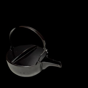 May include: A black, glossy teapot with a curved handle and a spout. The teapot has a rounded body and a lid with a handle. The background is solid black.