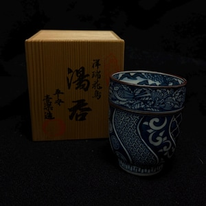 Può includere: Una tazza da tè giapponese blu e bianca con motivi intricati e un disegno di uccelli e fiori. La tazza è accanto a una scatola di legno con testo giapponese. La tazza è alta circa 7.6 cm.