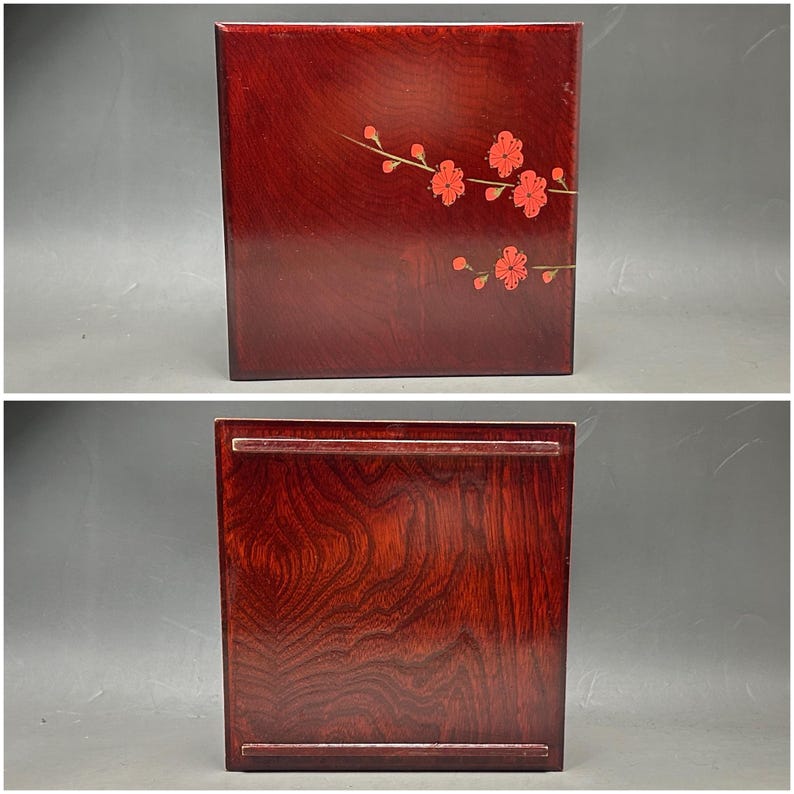 K&ouml;nnte beinhalten: Rechteckige, dunkelrote Holzbox mit floralem Design. Die Oberseite der Box zeigt einen Zweig mit roten Bl&uuml;ten. Die Unterseite der Box hat ein Tablett-&auml;hnliches Design. Die Holzmaserung ist sichtbar.