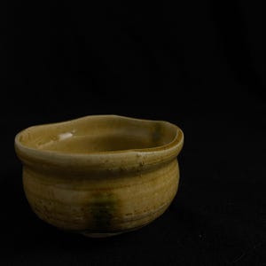 May include: A small, brown ceramic bowl with a slightly uneven rim. The bowl has a light brown glaze with streaks of darker brown and green.