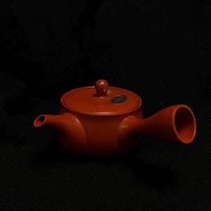 May include: A reddish-brown ceramic teapot with a side handle and a spout. The teapot has a lid with a small knob on top. The design is simple and elegant, suitable for serving tea. The teapot is set against a dark background.
