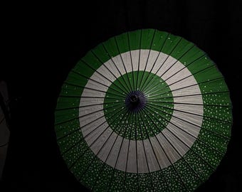 May include: A green and white patterned umbrella against a black background. The umbrella features a circular design with alternating green and white segments. The edges have a dotted pattern.