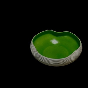以下が含まれることがあります： 鮮やかなライムグリーンの内側と、水平な溝が施された質感のある白い外側を持つ浅いボウル。ボウルの縁は独特の波打つような形状で、わずかな窪みがあり、暗い背景に対して曲線的な輪郭を描いています。