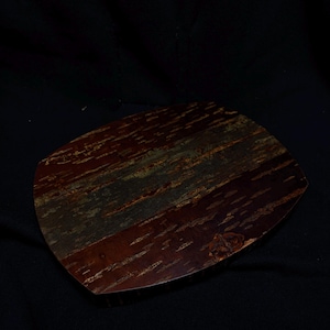 Peut inclure: Un plateau de service en bois de forme organique. Le plateau présente une couleur brun rougeâtre intense avec des stries vertes et dorées, créant un aspect naturel et texturé. Le grain du bois est visible, ajoutant au charme rustique de la pièce.