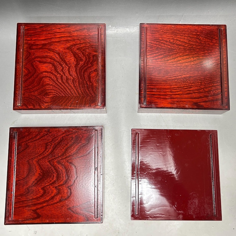 K&ouml;nnte beinhalten: Vier quadratische Holztabletts in einem satten, rotbraunen Farbton. Die Tabletts haben eine gl&auml;nzende Oberfl&auml;che und zeigen deutlich die Maserung des Holzes. Jedes Tablett hat einen vertieften Rand und eine glatte, polierte Oberfl&auml;che.