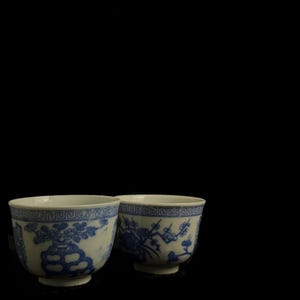 以下が含まれることがあります： 青と白の花柄が描かれた、小さな白い磁器製のティーカップが2つ。カップは伝統的な中国のデザインです。