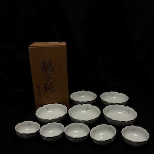 May include: A collection of ten white ceramic bowls with scalloped edges and floral accents, presented with a wooden box. The bowls feature delicate gray floral patterns. The wooden box has Japanese text.