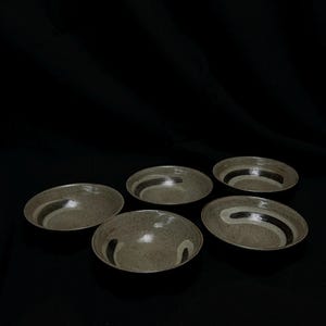 Puede incluir: Cinco cuencos de cerámica moteada con un diseño de rayas grises oscuras y blancas. Los cuencos tienen forma ovalada y tienen un borde ligeramente elevado. Los cuencos están colocados sobre una superficie negra.