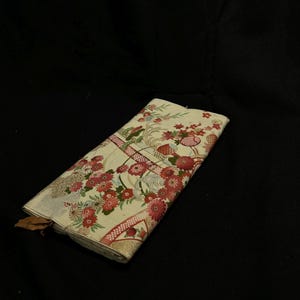 May include: Folded fabric featuring a floral pattern in red, pink, and cream. The design includes detailed flowers, leaves, and decorative borders. The fabric is neatly folded, displaying the intricate print.