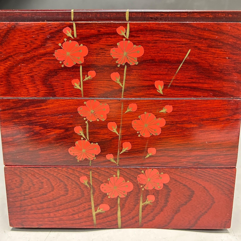 K&ouml;nnte beinhalten: Eine dreist&ouml;ckige, rote Holzkiste mit floralem Design. Die Kiste hat eine gl&auml;nzende Oberfl&auml;che und ist mit roten Bl&uuml;ten und goldenen Stielen verziert. Die Blumen sind in einem symmetrischen Muster angeordnet.