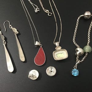 Puede incluir: Una colecci&oacute;n de joyas de plata que incluye pendientes, collares, una pulsera y pendientes de bot&oacute;n. Los collares presentan dise&ntilde;os de l&aacute;grima, cuadrados y colgantes. La pulsera tiene un dije de piedra preciosa azul. Los pendientes son largos.