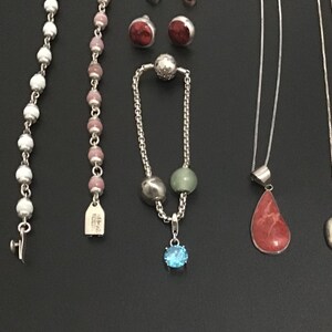 Puede incluir: Una variedad de piezas de joyer&iacute;a, incluyendo collares, pulseras y pendientes, se exhiben sobre una superficie oscura. La joyer&iacute;a presenta diversos dise&ntilde;os, incluyendo hilos de cuentas, colgantes de piedras preciosas y pendientes de bot&oacute;n.