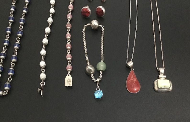 Puede incluir: Una variedad de piezas de joyer&iacute;a, incluyendo collares, pulseras y pendientes, se exhiben sobre una superficie oscura. La joyer&iacute;a presenta diversos dise&ntilde;os, incluyendo hilos de cuentas, colgantes de piedras preciosas y pendientes de bot&oacute;n.