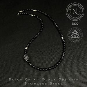 May include: A black onyx and obsidian necklace with stainless steel details. The necklace is made of small, round black beads and silver-coloured metal spacers. The pendant has an intricate pattern. The text "BLACK ONYX - BLACK OBSIDIAN STAINLESS STEEL" is at the bottom.