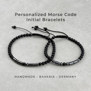 Könnte beinhalten: Zwei verstellbare Armbänder mit matten schwarzen Perlen und metallischen zylindrischen Abstandshaltern in Morsecode-Mustern. Der Text Personalized Morse Code Initial Bracelets und HANDMADE BAVARIA GERMANY ist im Bild zu sehen.
