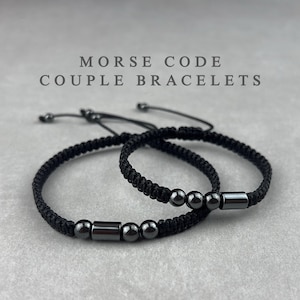 Peut inclure: Deux bracelets de couple en code Morse noirs. Les bracelets sont faits de cordon tressé noir et comportent des perles et des accents rectangulaires gris foncé. Le texte "MORSE CODE COUPLE BRACELETS" est affiché au-dessus des bracelets.