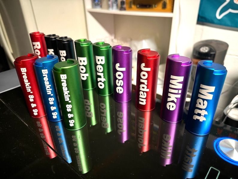 May include: A row of ten colourful metal containers with different names engraved on them, including "Matt", "Mike", "Jordan", "Jose", "Berto", "Bob", "Breakin' 8s & 9s", and "Ro".