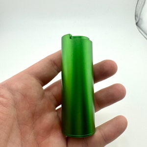 May include: A green metal cylinder with a smooth, matt finish. The cylinder has a small lip at the top.