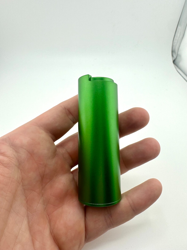May include: A green metal cylinder with a smooth, matt finish. The cylinder has a small lip at the top.