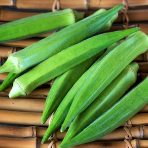 May include: A group of fresh green okra pods arranged on a woven bamboo surface.