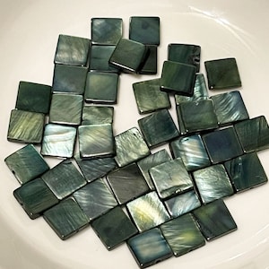 May include: A collection of dark green and black square-shaped iridescent tiles. The tiles are made of mother of pearl and have a smooth, polished finish.