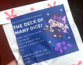Op de afbeelding: Een witte papieren zak met roze strikaccenten en een blauw label. Op het label staat "THE DECK OF MANY DICE!" en er staat een cartoon heks met dobbelstenen. De zak bevat een mystery dobbelstenenset.