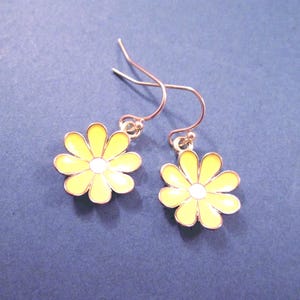 May include: A pair of daisy earrings with yellow petals and white centers. The earrings have a gold-colored metal frame and ear hooks. The earrings are set against a blue background.