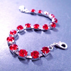May include: A silver-toned bracelet featuring a series of round, vibrant red faceted stones set in individual metal prongs. The bracelet includes a silver-toned lobster claw clasp and a short extender chain at one end for adjustable length.