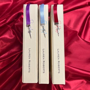 May include: Three hardcover books with matching ribbon bookmarks. Each bookmark has a silver charm in the shape of a sword. The books are all by the same author, Lauren Roberts.