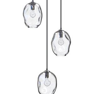 May include: Three clear glass pendant lights with black cords hanging from the ceiling. The glass is textured and has a slightly irregular shape.