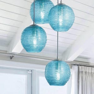 May include: Three blue glass pendant lights with a textured, rippled design hang from a white ceiling.