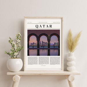 Puede incluir: Una impresión enmarcada de una ciudad vista a través de tres ventanas arqueadas. La ciudad está iluminada por la noche y se refleja en el agua debajo. La impresión tiene el título "Qatar" y el texto "No Place Like Home" en la parte superior.