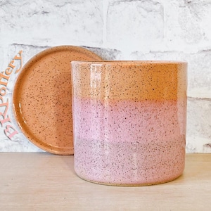 May include: A cylindrical ceramic planter with a matching saucer, featuring a speckled finish that transitions from a warm orange at the top to a soft pink at the base. The text BRPottery is visible in a light pink script on the left side.