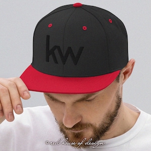 May include: A black and red flat-peak baseball cap featuring the embroidered letters "kw". The cap has a red peak and button, with red stitching on the crown. A classic, stylish accessory, suitable for various outfits.