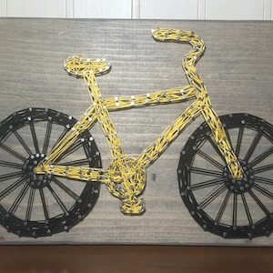 May include: A yellow bicycle made of string art on a gray wooden background.