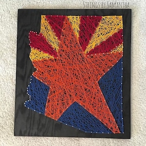 May include: String art of the state of Arizona with the state flag colors of red, yellow, and blue. The art is on a black wooden background. The text "STRINGS BY SAMANTHA" is at the top of the image.