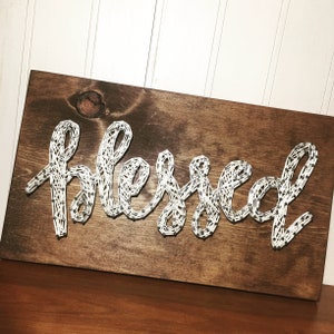 May include: A wooden sign with the word "Blessed" spelled out in white string wrapped around nails.