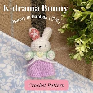 May include: Crochet pattern for a K-drama bunny wearing a traditional Korean hanbok (한복). The bunny is white with a pink flower on its head and is wearing a green and purple hanbok.