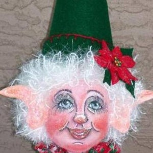 Puede incluir: Una muñeca de duende de Navidad hecha a mano con una peluca blanca rizada, un sombrero verde y una flor de poinsettia roja. El duende tiene una cara pintada con mejillas sonrosadas y una sonrisa amigable.