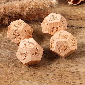 May include: Four wooden dice with engraved illustrations and text. Each die features different activities, including "Comedy," "Cook Together," "Movie Night," and "Burgers." The dice are light brown and have a geometric shape.