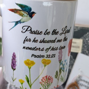 Pu&ograve; includere: Tazza in ceramica bianca con coperchio in bamb&ugrave;. La tazza presenta un design di uccello colorato e il testo "Lodato sia il Signore perch&eacute; mi ha mostrato le meraviglie del suo amore Salmo 31:21".